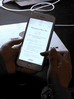 Hands holding an iPhone. On the screen the Slow Net Router's splash page displays the title 'Welcome to the Slow Net'.